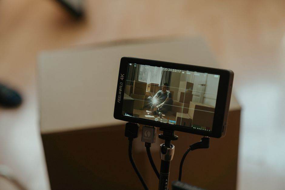 Mode Filmmaker sur TV en 2026 : réglages et limites A camera monitor shows a scene with a person sitting among boxes, highlighting the filming process.
