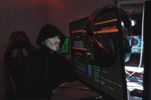 A person wearing a Guy Fawkes mask engaged in hacking activities on a computer in a dimly lit room.