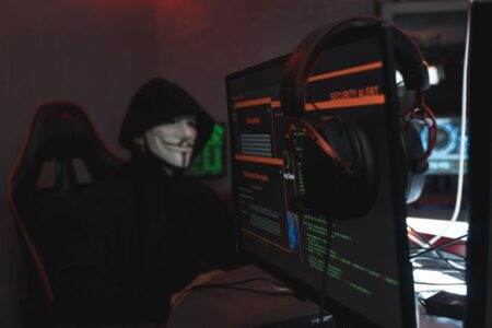 Fuite de données en 2026 : repérer les arnaques ciblées A person wearing a Guy Fawkes mask engaged in hacking activities on a computer in a dimly lit room.