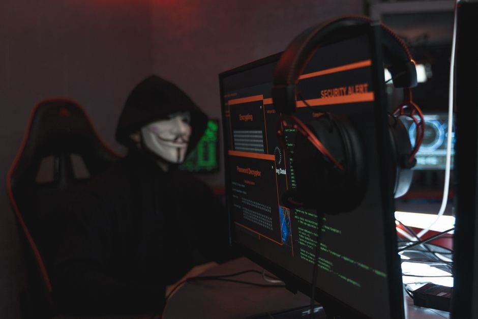 Fuite de données en 2026 : repérer les arnaques ciblées A person wearing a Guy Fawkes mask engaged in hacking activities on a computer in a dimly lit room.