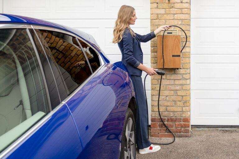 Voiture électrique en 2026 : autonomie, usage et seconde vie A woman efficiently charges her blue electric car at a home EV charging station.