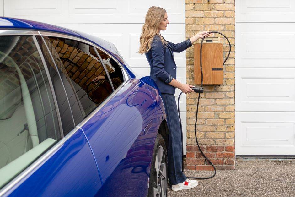 Voiture électrique en 2026 : autonomie, usage et seconde vie A woman efficiently charges her blue electric car at a home EV charging station.