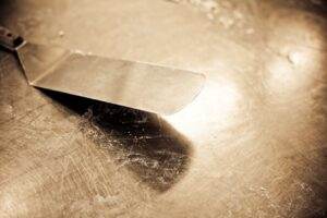 Close-up of a vintage stainless steel spatula on a worn countertop with sepia tones.