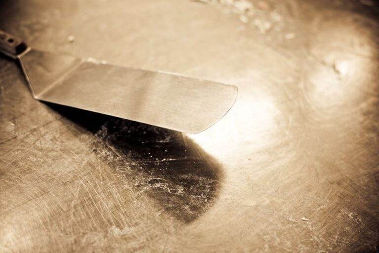 Une peinture auto-réparatrice ralentit la rouille en laboratoire Close-up of a vintage stainless steel spatula on a worn countertop with sepia tones.