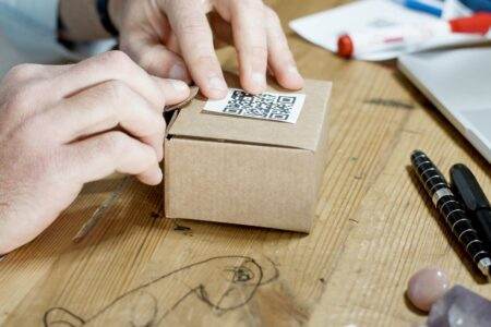 Codes en 2026 : cinq usages, cinq contextes Close-up of hands packing a box with a QR code, symbolizing online business services.