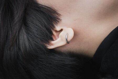 Casque à conduction osseuse, aide auditive, implant : trois usages à distinguer Detailed close-up of an ear featuring a silver hoop earring and black hair.