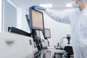 Researcher in PPE reviews data on a digital screen in a modern laboratory setting.