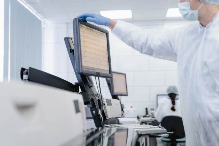 IA générative en santé : l’assistant ne porte pas la blouse Researcher in PPE reviews data on a digital screen in a modern laboratory setting.