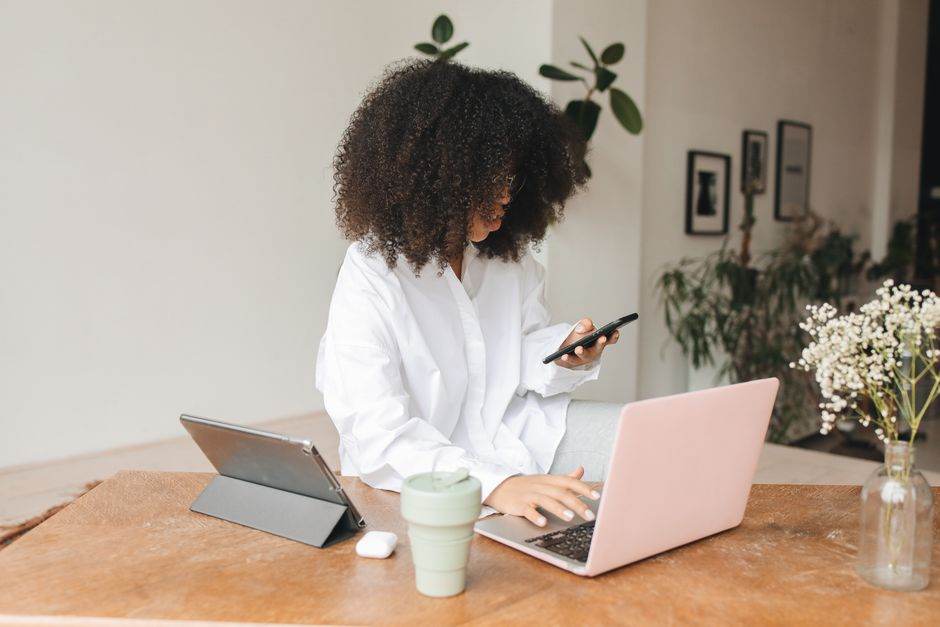 Young woman multitasking at home using laptop, tablet, and smartphone in a cozy indoor setting.