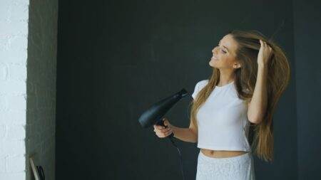 Shark FlexStyle IonCurl : ce que les réglages changent Young woman smiling while using a hairdryer for hair styling indoors.