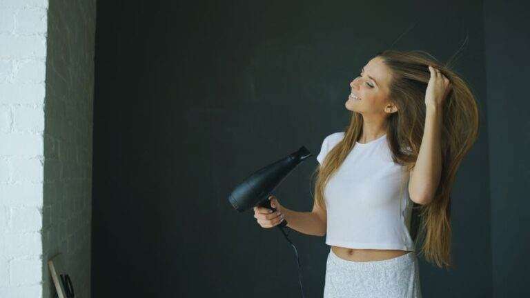 Young woman smiling while using a hairdryer for hair styling indoors.